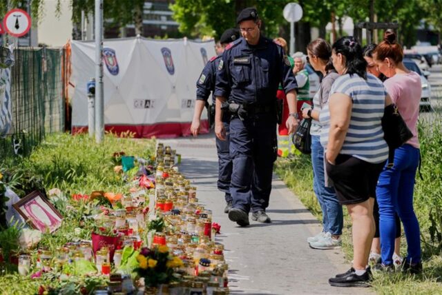 Menschen und Polizisten versammeln sich neben Kerzen und Blumen vor einer Schule in Graz, Österreich, wo ein ehemaliger Schüler zwei Tage zuvor das Feuer eröffnet hat.
