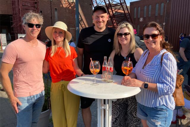 Drei Frauen und zwei Männer stehen bei der After-Work-Party am Imbiss am Schacht auf dem Gelände der Zeche Schlägel & Eisen in Herten-Langenbochum an einem Stehtisch nebeneinander.