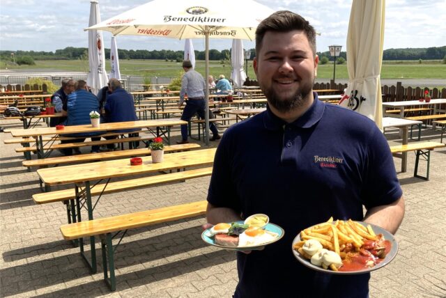 Ein Biergarten von außen mit einem großen Torbogen aus Holz.