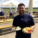Ein Biergarten von außen mit einem großen Torbogen aus Holz.