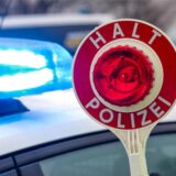 Ein Polizist hält eine Polizeikelle für eine Kontrolle vor einem Einsatzfahrzeug hoch.