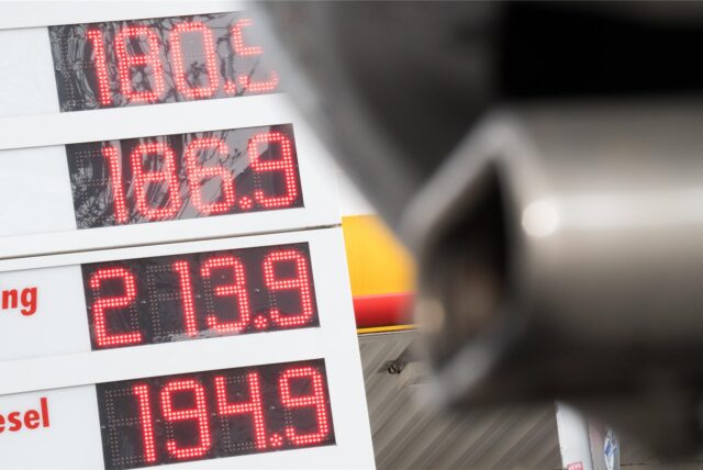 Die Preise für Diesel und Benzin E10 stehen an einer Tankstelle hinter einem parkenden Auto, dessen Auspuff im Vordergrund zu sehen ist.