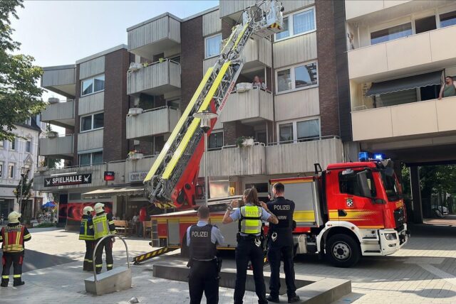 Ein Feuerwehrfahrzeug mit ausgefahrener Drehleiter vor einem Wohnhaus am Place d’Arras in Herten, davor weitere Einsatzkräfte.