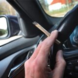 Ein Mann sitzt mit einem Joint zwischen den Fingern am Steuer eines Autos. (Symbolbild)