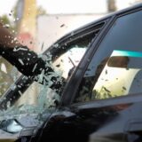 Ein Mann schlägt die Scheibe der Fahrertür eines Autos ein.