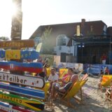 Menschen mit Liegestühlen auf einer Sandfläche auf einem Marktplatz.