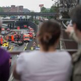 Menschen stehen auf einer Brücke und blicken runter auf einen Verkehrsunfall mit Rettungskräften und Rettungshubschrauber.