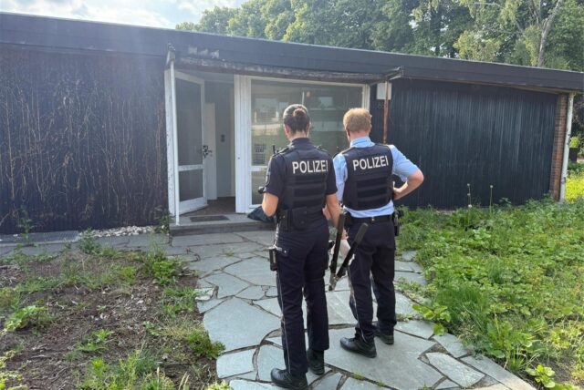 Polizisten stehen vor einem Haus, dessen Tür offen ist.