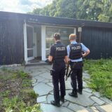 Polizisten stehen vor einem Haus, dessen Tür offen ist.
