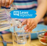Ein Kita-Kind gießt Wasser aus einer Kanne in ein Glas.