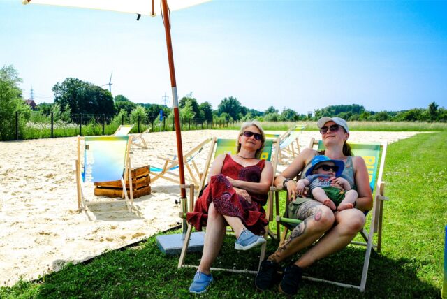 Zwei Frauen und ein kleines Kind sitzen auf Stühlen am Emscherstrand.