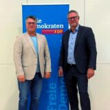 Zwei Männer im Sakko stehen vor einem Werbebanner der FDP.