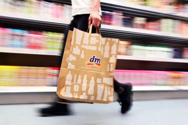Eine Person geht in einer Filiale der Drogeriemarktkette dm mit einer Tüte an einem Regal vorbei.