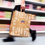Eine Person geht in einer Filiale der Drogeriemarktkette dm mit einer Tüte an einem Regal vorbei.