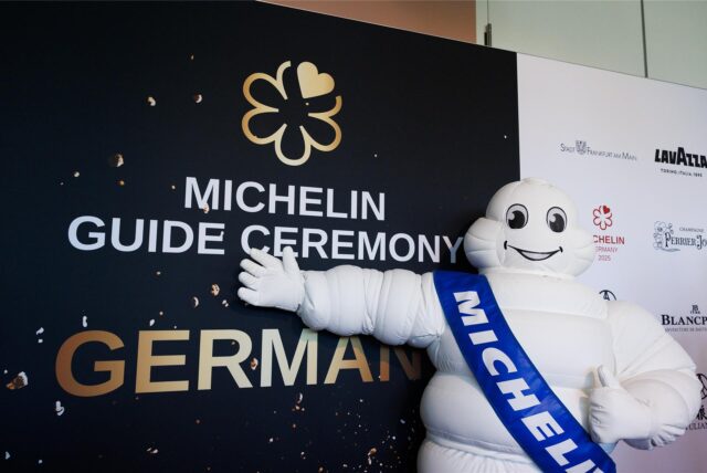 Das Michelin-Männchen steht vor einer Tafel mit der Aufschrift «Michelin Guide Ceremony Germany».