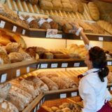 Eine Verkäuferin greift in einer Bäckerei und Konditorei in den Auslagen des Geschäfts nach einem Brot