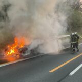 Feuerwehrleute löschen ein brennendes Auto auf einer Autobahn.