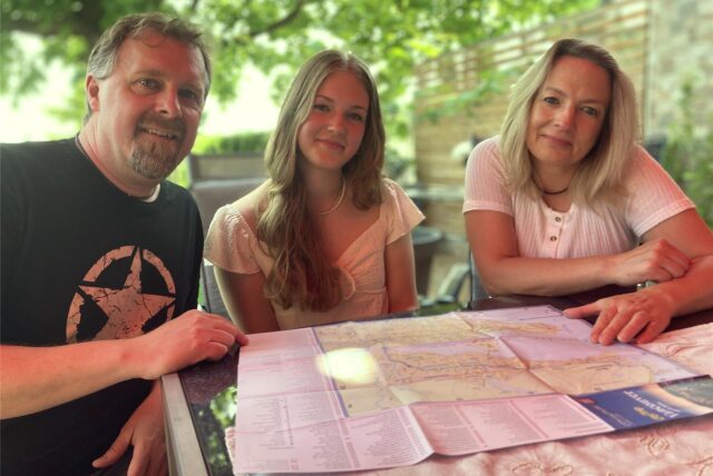 Elina Bartz sitzt mit ihren Eltern Ronald und Yvonne vor einer Landkarte von Vancouver.