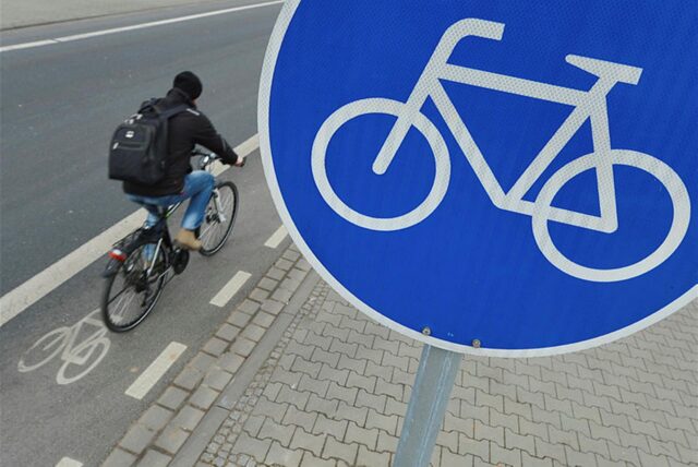 Radfahrer fährt auf einem Radweg an einem Radweg-Schild vorbei