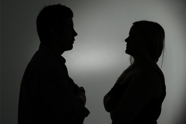 Ein als Silhouette abgebildeter Mann und eine Frau stehen sich mit verschränkten Armen gegenüber.