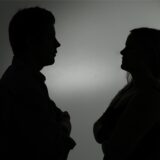 Ein als Silhouette abgebildeter Mann und eine Frau stehen sich mit verschränkten Armen gegenüber.