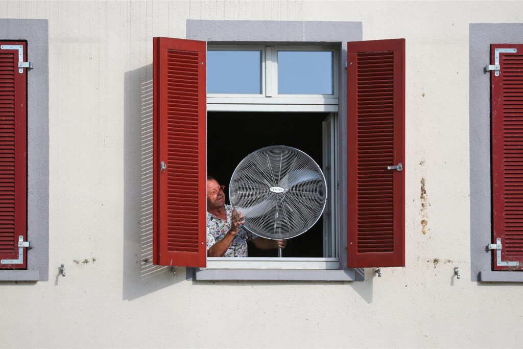 Ein Mann stellt am Morgen einen Ventilator an sein geöffnetes Fenster. Ein Mann stellt am Morgen einen Ventilator an sein geöffnetes Fenster.