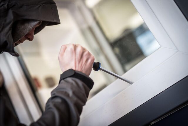 Ein Mann mit einem Schraubendreher hebelt ein Fenster auf.