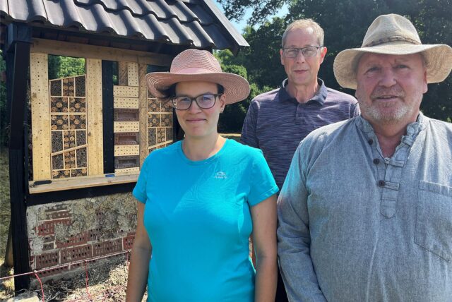 Eine Frau und zwei Männer stehen vor einem Wildbienenhotel.