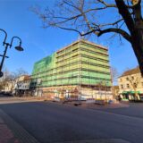 Ein Gebäude ist mit einem Gerüst und grünen Netzen umgeben. Baustellenabsperrungen sind im Vordergrund sichtbar.