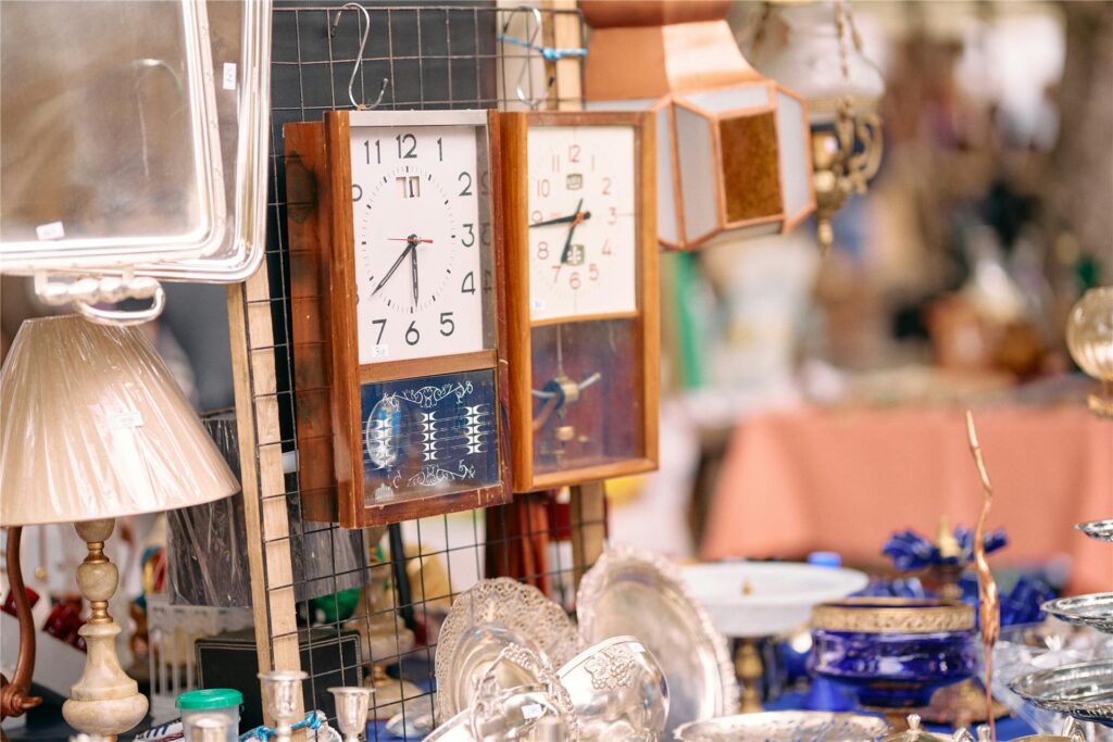An einem Trödelmarkt-Stand werden Uhren, Geschirr, Lampen, Deko und mehr angeboten. An einem Trödelmarkt-Stand werden Uhren, Geschirr, Lampen, Deko und mehr angeboten.