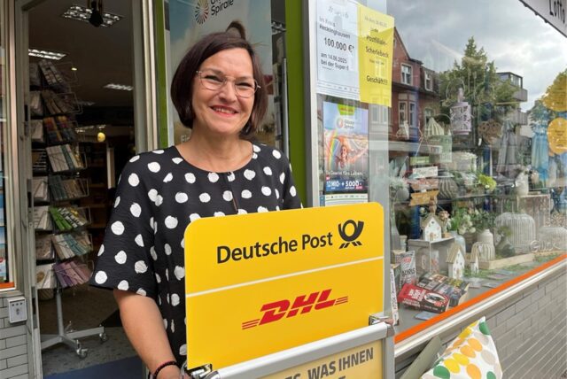 Sabine Hlava steht vor ihrem Geschäft mit einem Post-Kundenstopper in der Hand.