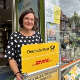 Sabine Hlava steht vor ihrem Geschäft mit einem Post-Kundenstopper in der Hand.