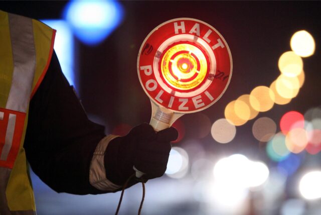 Ein Polizist hält nachts eine Kelle mit dem Aufdruck „Halt – Polizei“ in die Höhe. (Symbolbild)