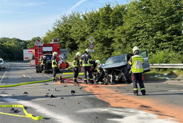 Feuerwehrleute stehen um ein Autowrack herum.
