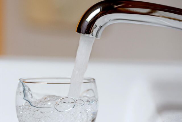 Wasser läuft aus einem Wasserkran in ein Glas.