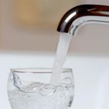 Wasser läuft aus einem Wasserkran in ein Glas.