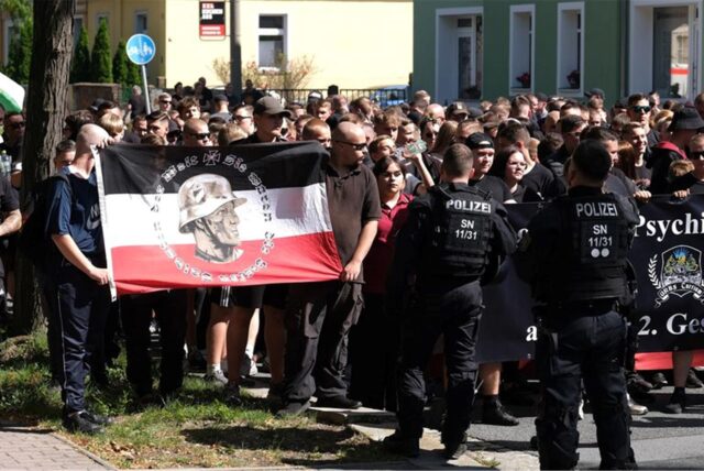 Teilnehmer einer rechtsextremen Demonstration werden von Polizisten begleitet.