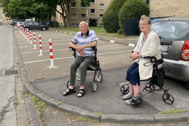 Zwei Senioren sitzen auf Rollatoren vor einem Parkplatz in Marl.