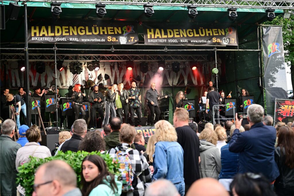 Menschen stehen vor einer Bühne, auf der das Rock Orchester Ruhrgebeat spielt. Menschen stehen vor einer Bühne, auf der das Rock Orchester Ruhrgebeat spielt.