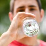 Ein Mann trinkt stilles Mineralwasser aus einer Glasflasche.