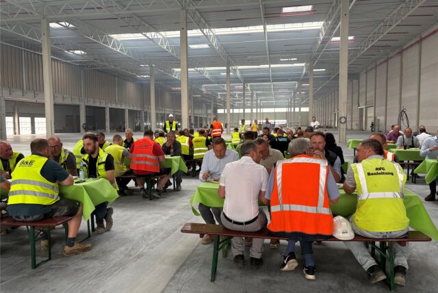 In der großen Thalia-Halle sitzen Arbeiter an Tischen mit grünen Tischdecken, einige von ihnen tragen Warnwesten.