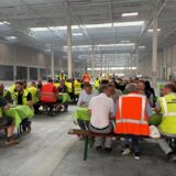 In der großen Thalia-Halle sitzen Arbeiter an Tischen mit grünen Tischdecken, einige von ihnen tragen Warnwesten.