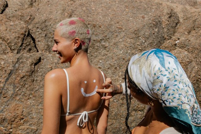 Eine Frau cremt einer anderen Frau den Rücken mit Sonnencreme ein.