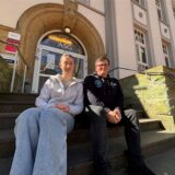 Pia Cramer und Felix Koch sitzen auf den Treppenstufen vor der Schultür des Adalbert-Stifter-Gymnasiums in Castrop-Rauxel.