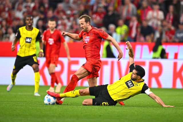 Spielszene aus einem Fußballspiel zwischen Bayern München (in Rot) und Borussia Dortmund (in Gelb), ein Dortmunder Spieler grätscht gegen einen Bayern-Spieler um den Ball.