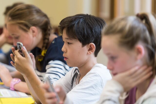 Drei Schüler in einem Klassenraum, die alle auf ihre Handys schauen.
