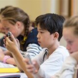Drei Schüler in einem Klassenraum, die alle auf ihre Handys schauen.