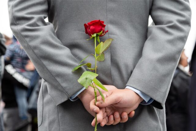 Ein Mann hält eine Rose hinter dem Rücken.