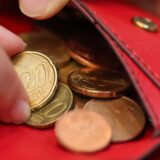 Das Bild zeigt eine Collage. Links ist ein rotes Portemonnaie mit einigen Euro-Cent-Münzen zu sehen, wobei eine Hand nach einer 20-Cent-Münze greift. Rechts ist ein Schlagloch in einer asphaltierten Oberfläche zu sehen, das mit Wasser gefüllt ist.