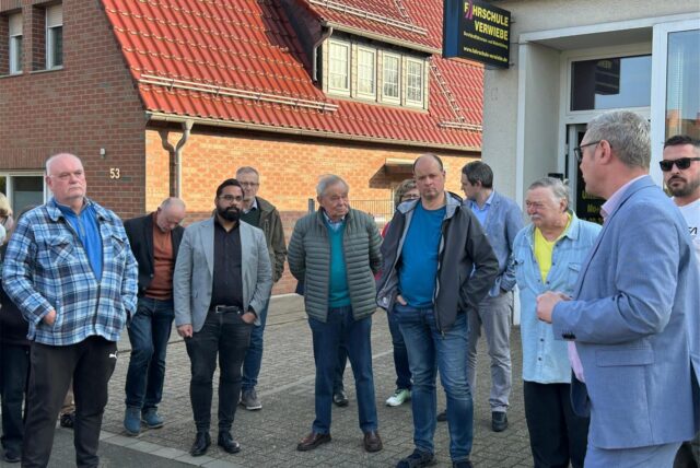 Eine Gruppe von Männern steht zusammen. Die Personen sind unterschiedlich gekleidet und scheinen sich zu unterhalten.